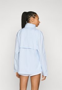 Chaqueta de chándal azul claro con un cuello alto, de corte oversize y espalda corta. Fabricada con tejido liso y ligero, con mangas largas.