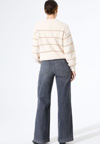 Pull rayé crème avec une texture douce et un col rond, associé à un jean taille haute à jambes larges de couleur foncée avec des poches arrière.
