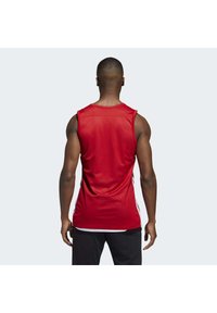 Débardeur de sport rouge en tissu léger, avec un col rond et des accents de rayures blanches sur les côtés, au design ajusté.