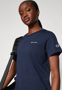 Navyblauwe katoenen t-shirt met korte mouwen, voorzien van een klein wit "Champion" logo op de linkerborst en een logo op de mouw.