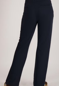 Marineblauwe broek met brede pijpen en een gladde textuur, voorzien van twee achterzakken en een taille met middenhoogte. Het ontwerp legt de nadruk op comfort en veelzijdigheid.