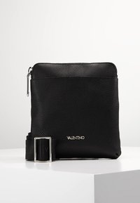 Svart läder crossbody-väska med en strukturerad yta, utrustad med en silverfärgad dragkedja och en märkesbälte. Kompakt rektangulär design.