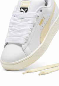 Bijela tenisica s teksturiranim sintetičkim gornjim dijelom, sa bež PUMA prugom, debelim bijelim vezicama i gumenim potplatom s prepoznatljivim uzorkom.
