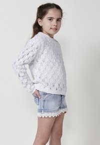 Pull en tricot blanc avec un motif texturé et un col rond, associé à un short en denim bleu clair avec un bord en dentelle.