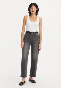 Aukštos juosmens tiesios tamsiai pilkos džinsai su juodu diržu. Prigludusi balta dryžuota maikutė ir juodi plokšti bateliai užbaigia įvaizdį.