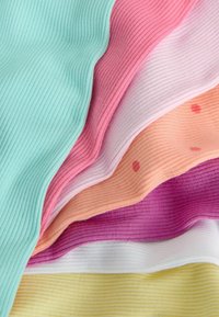 Pile de couches de tissu doux et côtelé dans des couleurs pastel : bleu sarcelle, rose, violet clair, pêche avec des taches rouges, violet, blanc et jaune pâle.