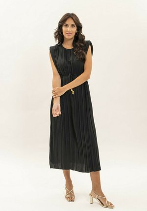 Robe midi plissée noire avec des manches courtes, encolure froncée et ceinture à la taille. Assortie avec des talons à lanières métalliques pour le contraste.