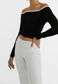Zwart geribbeld off-the-shoulder langemouwtop met een witte rand, gecombineerd met lichtgrijze high-waisted leggings; gladde textuur.