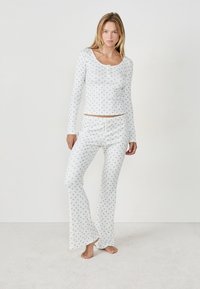 Conjunto de pijama de algodón blanco que incluye una camiseta de manga larga con un pequeño estampado floral azul y pantalones acampanados a juego con una cintura ajustable de cordón.