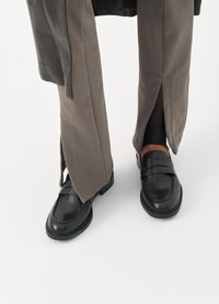 Black leather loafers with a strap detail, paired with gray corduroy pants featuring side slits. Smooth texture and classic design.