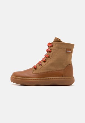 Bottes montantes à lacets en toile et cuir, de couleur beige, avec des lacets orange, bout rond et semelle en caoutchouc texturé.