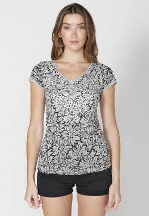 T-shirt gris à manches courtes avec un motif floral noir, présentant un col en V et un accent floral texturé au centre.
