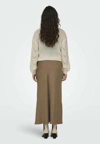 Pull en tricot crème avec des manches ballons, assorti d'une longue jupe marron, mettant en valeur une texture lisse et une silhouette élégante.