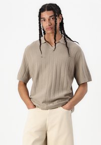 Camisa polo de manga corta en color beige con textura de canalé vertical y diseño de cuello en V. Tejido ligero con corte suelto y detalles sutiles.
