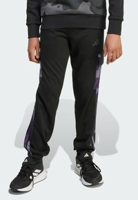 Black athletic pants featuring purple side stripes, elastic waistband, and cuffed ankles, paired with black training shoes with white accents.