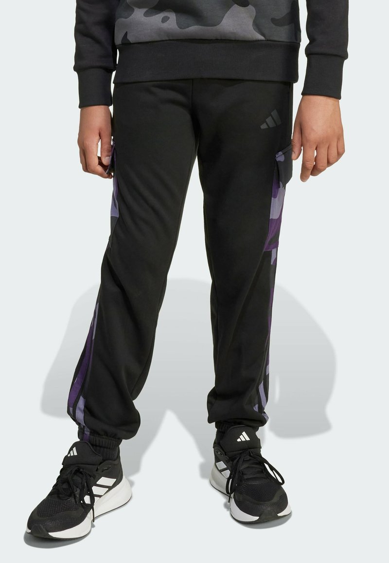Black athletic pants featuring purple side stripes, elastic waistband, and cuffed ankles, paired with black training shoes with white accents.