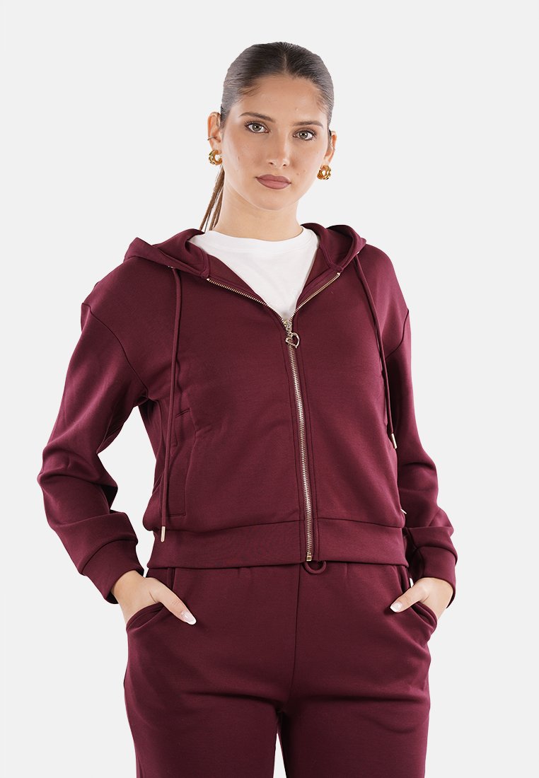 Felpa con zip color bordeaux, dotata di tasca a marsupio, polsini a coste e cappuccio regolabile con lacci. Realizzata in materiale morbido con una texture liscia.
