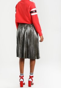 Sudadera corta roja con rayas blancas y negras en las mangas, falda plateada plisada metálica y sandalias de tacón rojas con calcetines blancos hasta el tobillo.