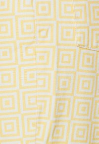 Tecido amarelo e branco com padrão geométrico de quadrados, apresentando um tecido texturizado para uma dimensão adicional.