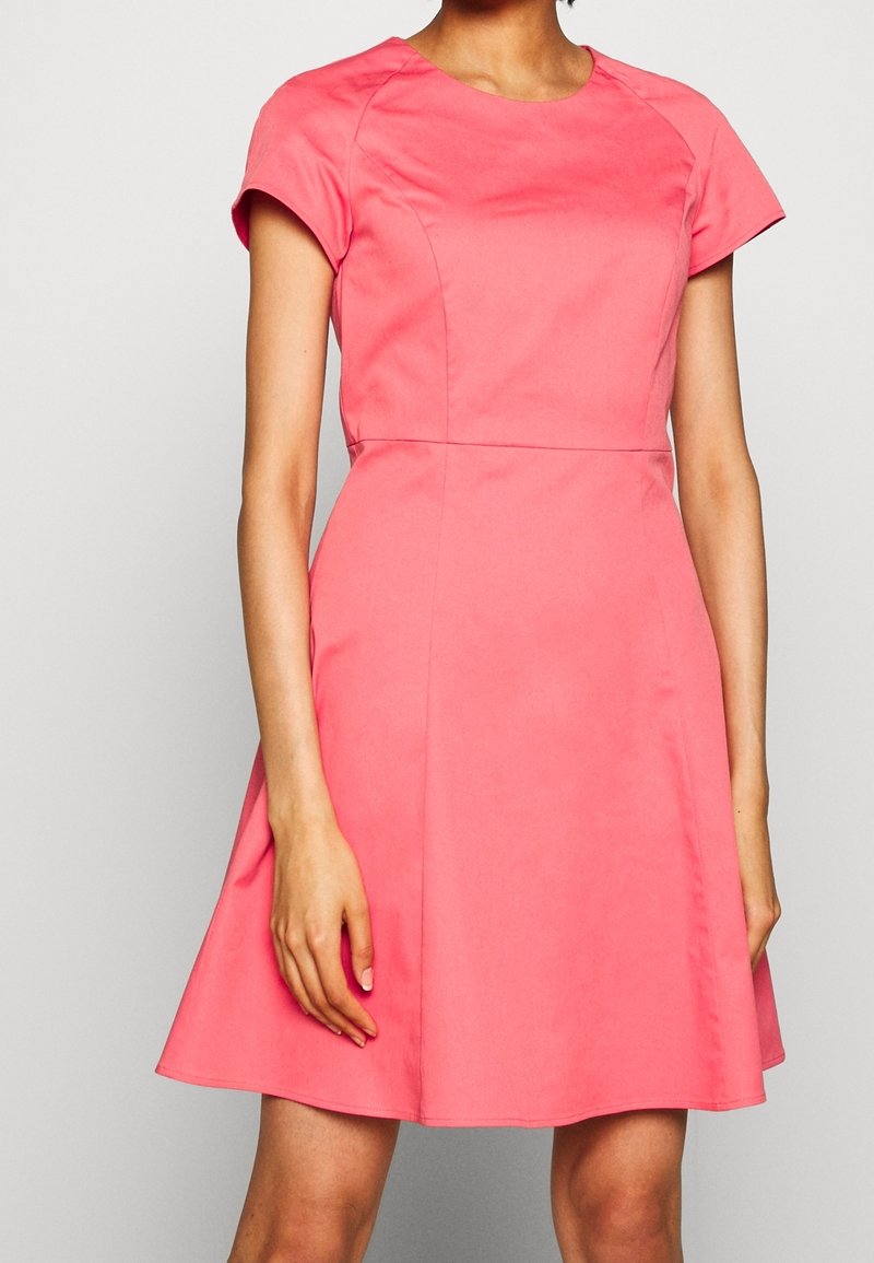 Robe corail à manches courtes avec un corsage ajusté et une jupe évasée, en tissu lisse, avec un col rond et des détails de couture subtils.