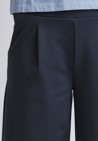 Donkerblauwe broek van zachte stof, met voorplooien en een gladde textuur, gecombineerd met een lichtblauw T-shirt net boven de taille.