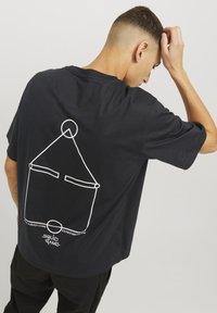 Sort bomulds t-shirt med et hvidt geometrisk design og tekst på bagsiden. Korte ærmer og en løs pasform, med rund halsudskæring.