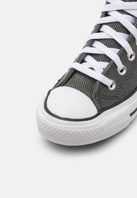 Gray canvas sneaker with white laces, white rubber toe cap, and textured side panels. Features black trim and diamond-patterned rubber sole.
