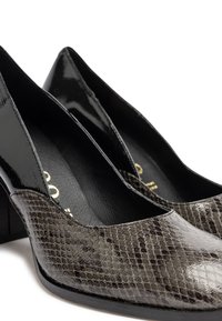 Scarpe nere con tacco a punta, con una finitura lucida e una texture in pelle di serpente in tonalità grigie e nere. Materiali texturizzati e lisci.