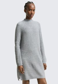 Robe pull côtelée grise avec un col haut, des manches longues et des fentes sur le bas ; texture douce et silhouette ajustée.