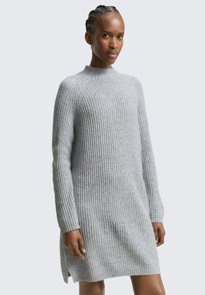 Graues, geripptes Strickkleid mit hohem Kragen, langen Ärmeln und seitlichen Schlitzen am Saum; weiche Textur und figurbetonte Silhouette.