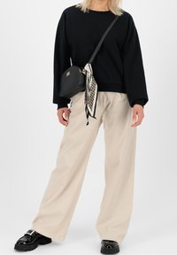 Musta collegepaita, leveät beige housut, musta käsilaukku kuvioidulla huivilla. Massiiviset mustat kengät. Rennon istuvuuden omaava arkiasu.