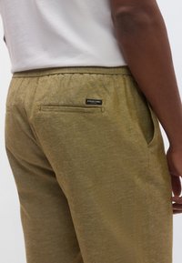 Φόρμα ελιάς από υφή υφάσματος, με πίσω τσέπη και μικρή ετικέτα με το εμπορικό σήμα στη μέση. Ελαστική μέση.