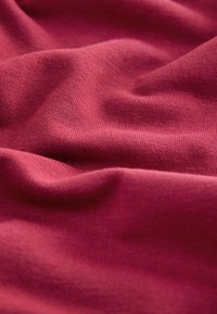 Primo piano di tessuto rosso morbido e strutturato con motivo a maglia visibile e pieghe delicate che creano contrasti di luce e ombra.