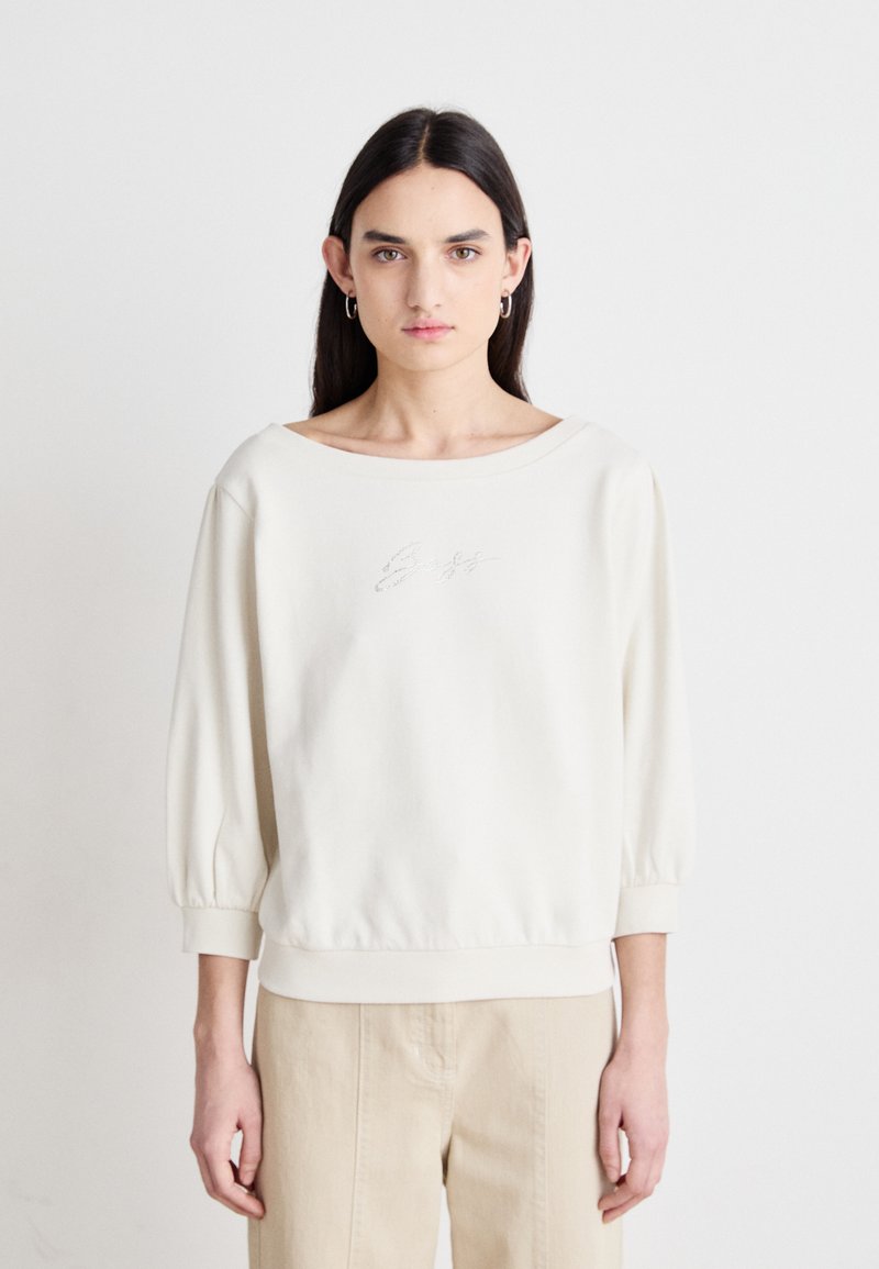 Lichtbeige sweatshirt met ronde hals, met 3/4 lange pofmouwen en ribbumboorden. Heeft subtiele geborduurde details aan de voorkant.