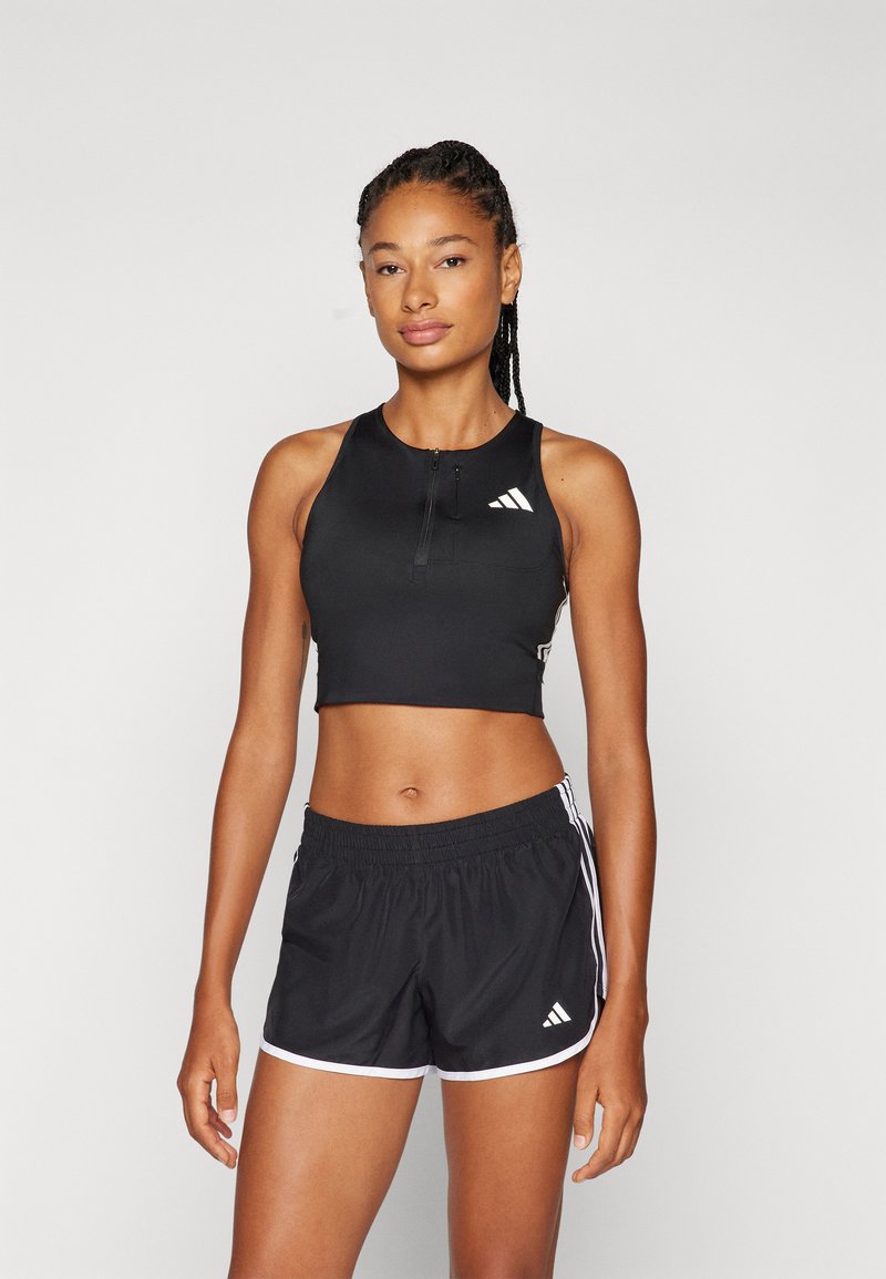 Melnas sportiskas crop top ar priekšējo rāvējslēdzēju un baltām logo akcentiem, kombinēts ar melnām šortiem ar baltām sānu svītrām un elastīgu jostasvīru.
