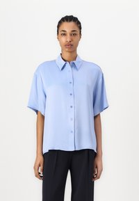 Light blue short-sleeve shirt with a button-down front and relaxed fit. Smooth texture, classic collar, and softly curved hem.