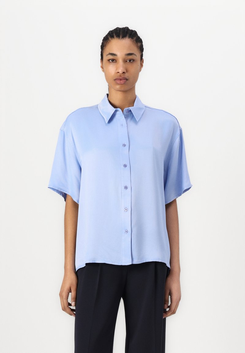 Light blue short-sleeve shirt with a button-down front and relaxed fit. Smooth texture, classic collar, and softly curved hem.