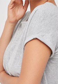 Lys grå kortærmet t-shirt lavet af blødt stof. Har en rund halsudskæring og opkrøllede manchetter, med en glat, tekstureret overflade.