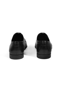 Zwarte leren schoenen met een gladde textuur, ronde neus en lage hak, weergegeven vanaf de achterkant met minimale ontwerpelementen.