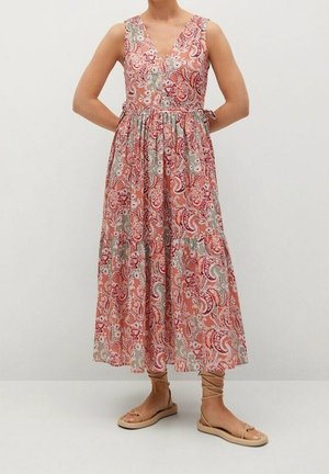 Kvinde iført en ærmeløs V-hals, ankellang kjole med pink, rød og grå blomster-paisley-mønster og beige snøresandaler med flad hæl.