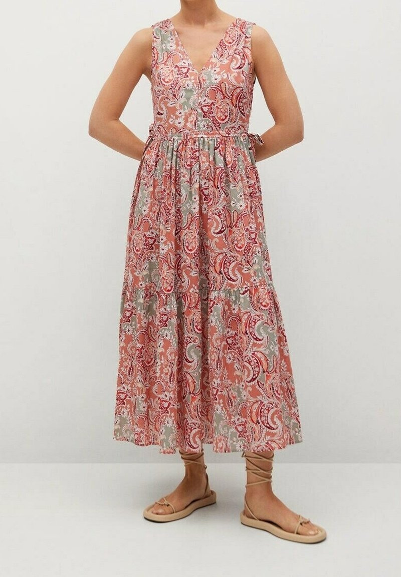 Femme portant une robe sans manches à col en V, longueur cheville, avec un motif floral paisley rose, rouge et gris, et des sandales plates beiges à lacets.