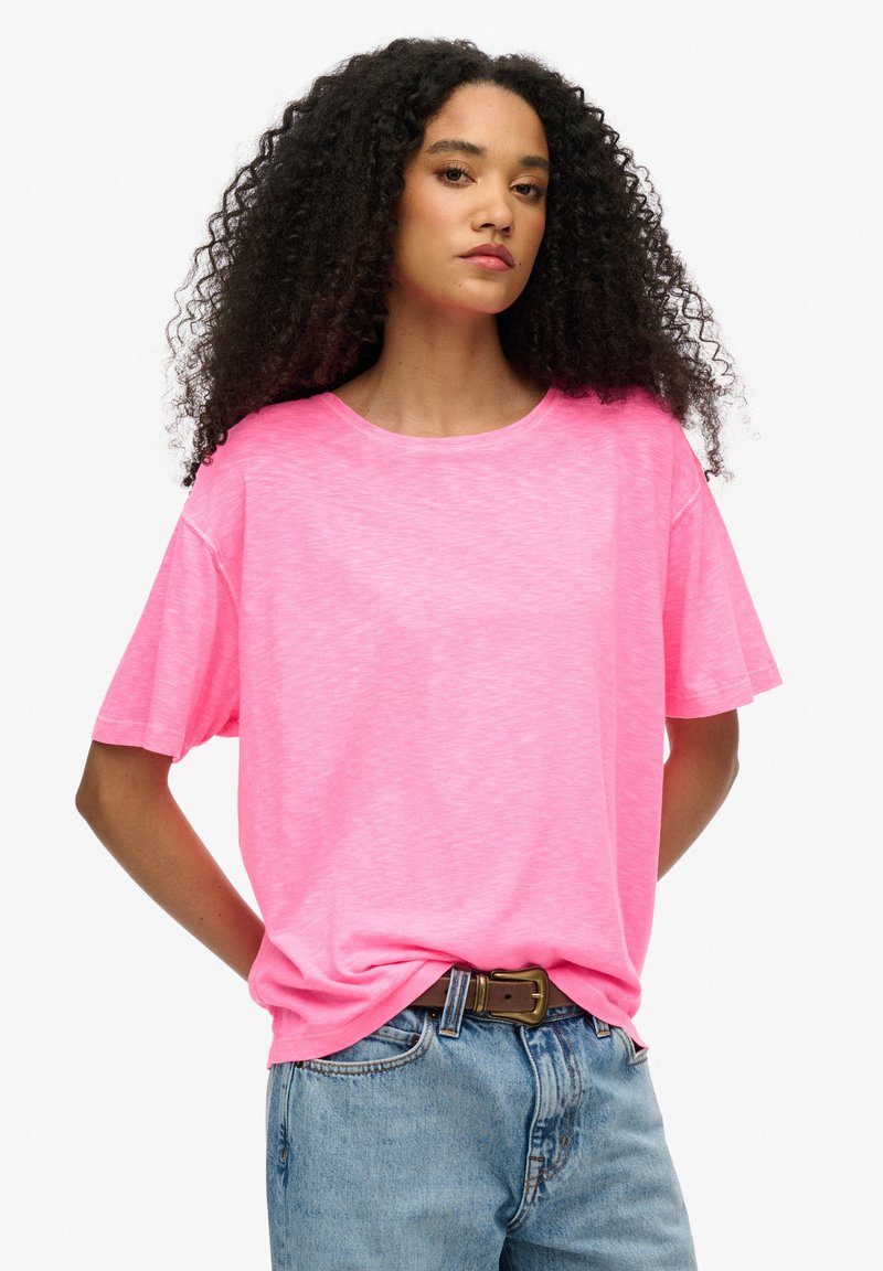 Camiseta de manga corta de color rosa brillante, hecha de una tela ligera, con escote redondo y corte relajado, combinada con jeans de mezclilla azul claro.