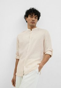 Camisa de botones de rayas melocotón claro con cuello mao, mangas enrollables y corte recto, combinada con pantalones de color claro.