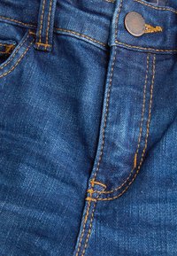 Jeans i denim med en mörkblå nyans, kontrasterande gul sömnad, en framficka och en metallknapp vid midjan.