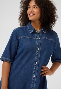 Robe en denim à manches courtes, de couleur bleu moyen, avec un col, des boutons sur le devant et des détails de couture.