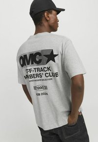Camiseta de algodón gris con texto gráfico negro en negrita y motivo de estrella en la parte posterior, manga corta y un corte relajado.