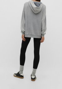 Hoodie grigia oversize con cappuccio regolabile, abbinata a leggings neri e sneakers nere con dettagli bianchi e calze grigie a trama.