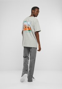 Grå grafisk T-skjorte med et trykk av ørkenlandskap på baksiden, parret med grå vide bukser og hvite sneakers.