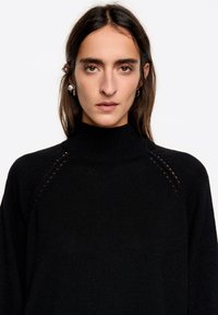 Czarny sweter dziany z wysokim kołnierzem, prążkowaną fakturą i ażurowymi detalami na ramionach. Luźny fason.