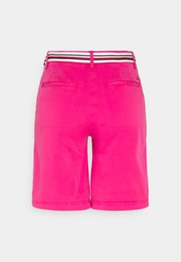 Pantaloni corti rosa con una texture liscia, dotati di una vita a strisce in nero, bianco e rosso. Sono visibili le tasche posteriori, con un taglio dritto.